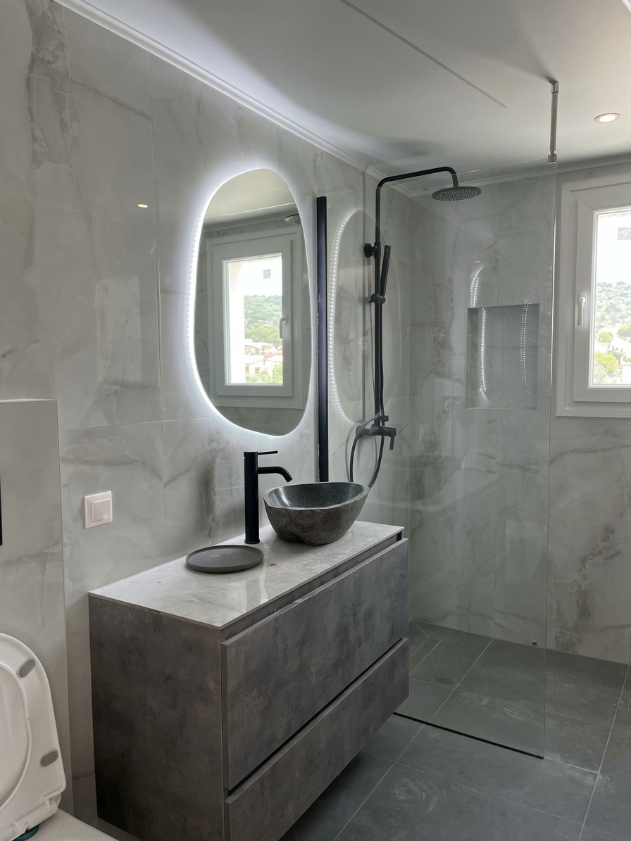 Modern bathroom with marble vanity, oval backlit mirror, black faucet, and glass shower enclosure.