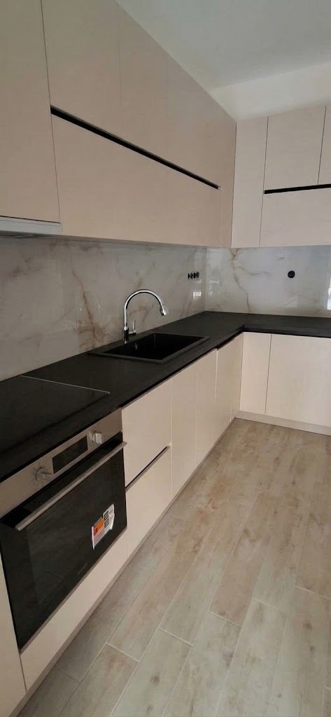 Modern L-shaped kitchen with dark countertops, white cabinets, marble backsplash, and stainless sink and faucet.